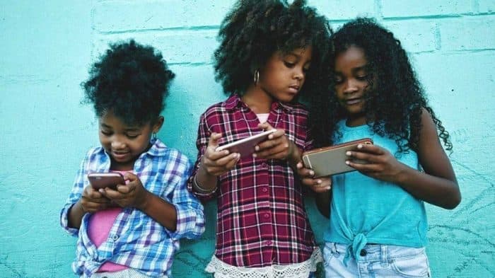 3 kids against a wall using smartphones