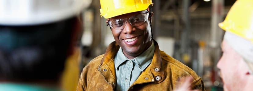 Man wearing construction clothing smiling in a yellow hsard hat